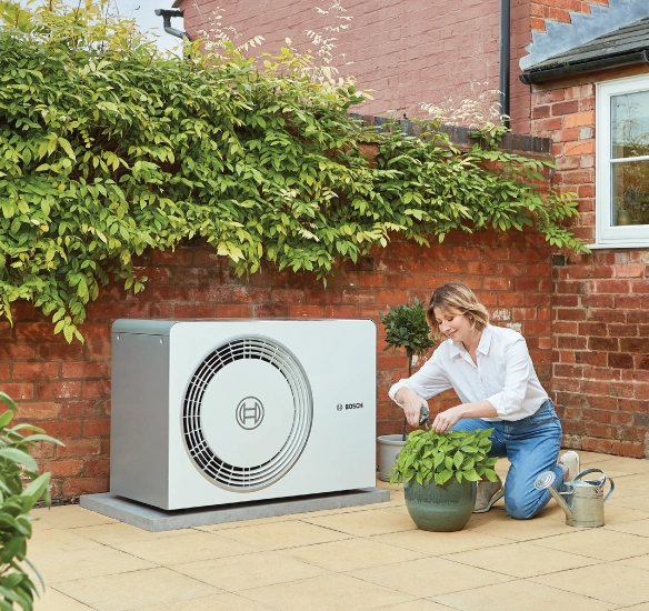 Woman tending to a plant next to the 5800 heat pump outdoors